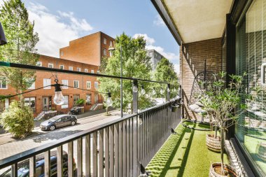 Dar tuğlalı balkon, metal parmaklıklar, tahta sandalye ve kapı.