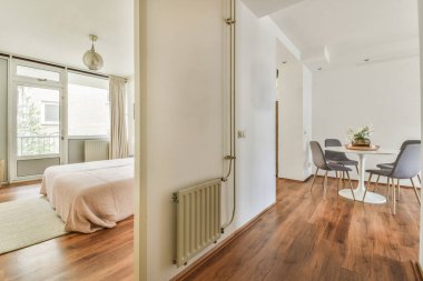 Çağdaş dairenin geniş odasındaki dinlenme odası ve yatak odası yakınlarındaki sandalyeli ve çiçekli masa.