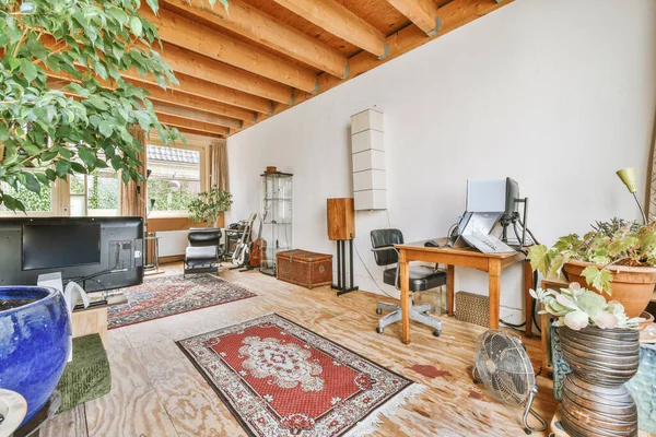 Interior of spacious apartment room on attic of building furnished with gray sofa and dining table with ladder leading upstairs