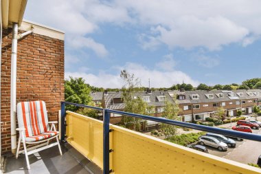 Dar tuğlalı balkon, metal parmaklıklar, tahta sandalye ve kapı.