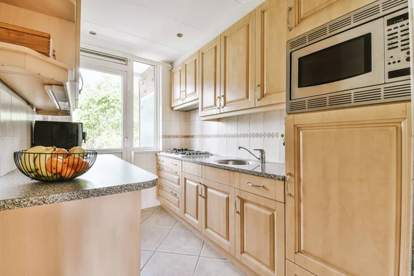 Well organized small home kitchen interior with sink under window and light furniture with stove and fridge in urban apartment