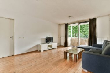 Yumuşak rahat kanepenin ve televizyonun yanındaki konforlu oturma odasının penceresinin yanındaki dikdörtgen masa ve lamba.