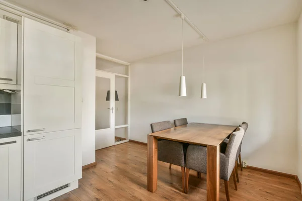 Modern minimalist style interior design of studio apartment with open white kitchen and dining zone with table and chairs illuminated by loft style lamp