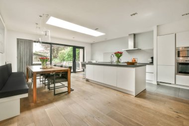 Çağdaş dairenin geniş odasındaki dinlenme odası ve mutfağın yakınındaki sandalyeli ve çiçekli masa.