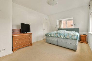 Comfortable bed with white bedclothes and bedside table with lamp placed near window in light bedroom at home