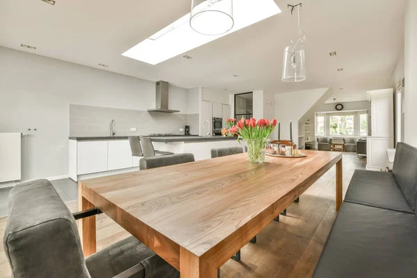 Çağdaş dairenin geniş odasındaki dinlenme odası ve mutfağın yakınındaki sandalyeli ve çiçekli masa.