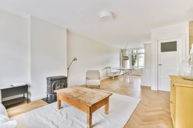 Sandalyeleri ve vazosu olan eski püskü ahşap masa modern apartmanda dekorasyonlu aydınlık duvarlara karşı rahat kanepenin yanında.