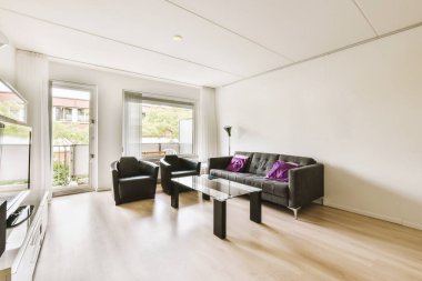 Modern apartmandaki dekorasyonlu ve televizyonlu, rahat koltuğun yanına yerleştirilmiş eski püskü ahşap masa.