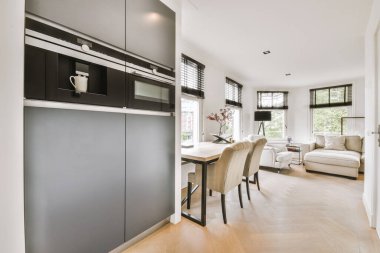 Günümüz minimalist tasarımı. Hafif stüdyo dairesinin ahşap masası ve oturma odası ile beyaz duvarları ve parke zemini arasında yemek masası ve sandalyeleri var.