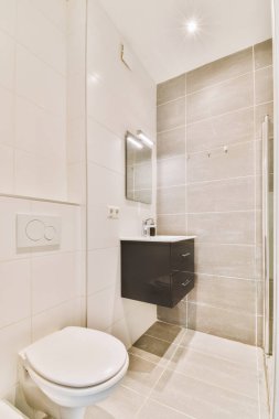 Modern sifon tuvaleti ve seramik lavabo aynanın yanındaki beyaz fayanslı duvarlara ve evdeki küçük tuvaletteki havluya monte edildi.