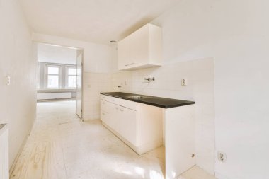 Pencereleri ve ahşap parke zemini olan boş beyaz mutfağın içi.