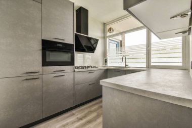 Gündüz vakti modern bir dairede yemek odasının yakınında modern dolaplar ve aletlerle donatılmış aydınlık mutfağın içi.