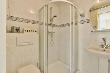 Evdeki modern tuvalette asılı duran banyo musluğu ile duvar arasındaki cam bölme.