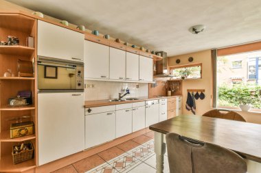 Gündüz vakti modern bir dairede yemek odasının yakınında modern dolaplar ve aletlerle donatılmış aydınlık mutfağın içi.