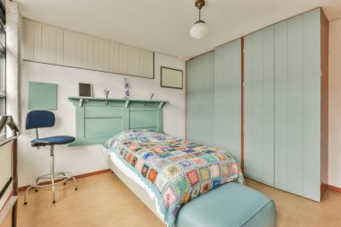 Dolapların yanında benekli yorgan ve minimalist tarzda modern bir dairede minimalist yatak odasında sandalyeli bir masa.