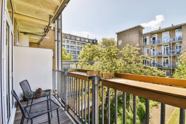 Dar tuğlalı balkon, metal parmaklıklar, tahta sandalye ve kapı.