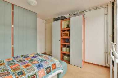 Dolapların yanında benekli yorgan ve minimalist tarzda modern bir dairede minimalist yatak odasında sandalyeli bir masa.