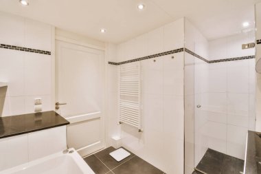 Aynalı lavabo ve temiz küvet modern banyoda cam kapılı ve beyaz fayanslı duvarları olan duş kutusunun yanında.