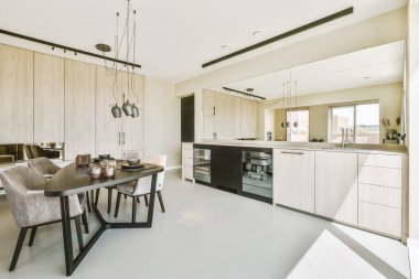 Stüdyo dairesinin modern minimalist tarzı iç tasarımı açık beyaz mutfak ve yemek masası ve sandalyeleri tavan arası lambasıyla aydınlatılmış.