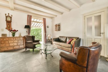 Çağdaş dairenin geniş odasındaki dinlenme odası ve mutfağın yakınındaki sandalyeli ve çiçekli masa.