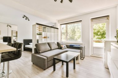 Günümüz minimalist tasarımı. Hafif stüdyo dairesinin ahşap masası ve oturma odası ile beyaz duvarları ve parke zemini arasında yemek masası ve sandalyeleri var.
