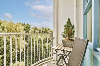 Narrow brick balcony with metal railings, wooden chair and door