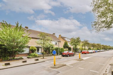 Arabaları, ağaçları ve fenerleri olan boş bir kaldırımdan panorama manzaralı evler.