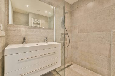 Evdeki modern tuvalette asılı duran banyo musluğu ile duvar arasındaki cam bölme.