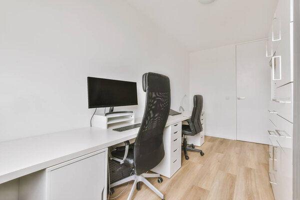 Comfortable chair placed near desk with computer monitors and whiteboard in light workplace in modern apartment