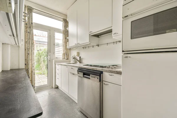 Modern home kitchen corner interior design with white cupboards and cabinets and steel hood over stove in contemporary apartment