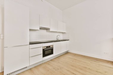 Pencereleri ve ahşap parke zemini olan boş beyaz mutfağın içi.