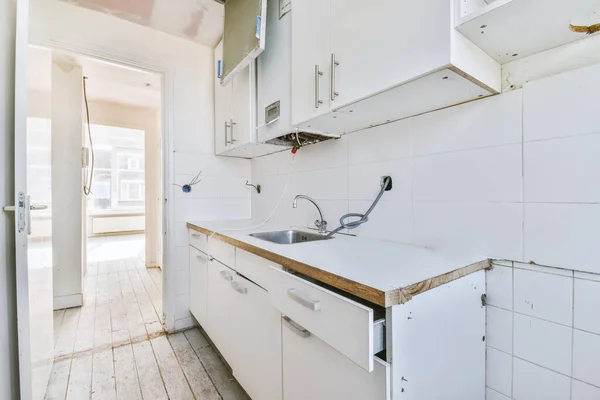 Well organized small home kitchen interior with sink under window and light furniture with stove and fridge in urban apartment