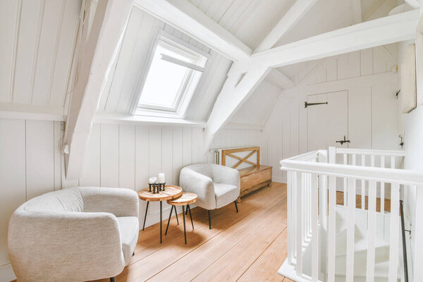 Interior of white room with baby crib and armchair near window with blue chest of drawers in daylight