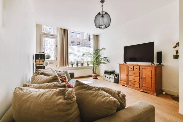 Çağdaş dairenin pencerelerine karşı rahat kanepesi ve televizyonu olan oturma odası.