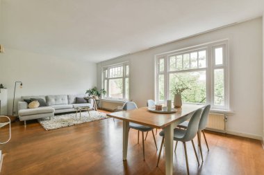 Yumuşak yastıklı büyük köşeli kanepe yemek odasının yanındaki açık oturma odasındaki elektrikli şöminenin yanındaki zarif avizenin altında.