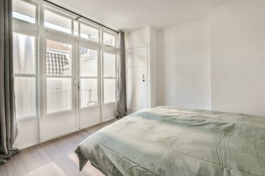 Balkon kapısının yanında rahat bir yatak, evdeki rahat yatak odasında perdeler var.