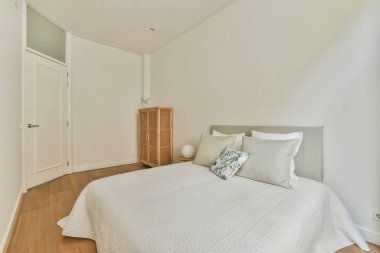 Yorgan ve yastıklarla dolu rahat bir yatak sandalye ve duvarın yanında çerçeveli bir tablo aydınlanmış yatak odasındaki gardıroba karşı.