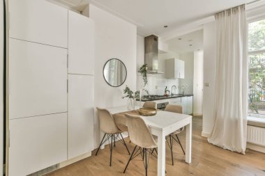 Çağdaş dairenin geniş odasındaki dinlenme odası ve mutfağın yakınındaki sandalyeli ve çiçekli masa.