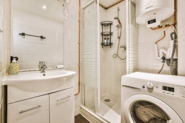 Modern banyoda aynalı lavabo ve cam kapılı duş kutusu ve beyaz fayanslı duvarlar.