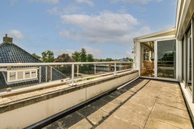 Metal parmaklıklı tuğla balkon, tahta sandalye ve camlı kapı mutfağa açılıyor.