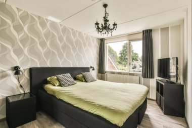 Rahat yataklı ve yumuşak yastıklı modern bir yatak. Yatağın yanındaki komodinin yanında ve geniş yatak odasındaki televizyonun yanında.