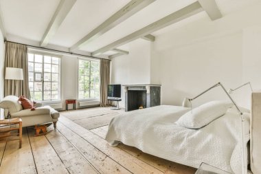 Rahat yatak ve şömine, modern apartmanda beyaz duvarları ve televizyonu olan minimalist tarzda bir yatak odasına yerleştirildi.