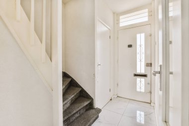 Kapalı beyaz oda kapısı çerçeveli resimlerin yanında ve evdeki merdivenin tepesinde şık bir lamba var.