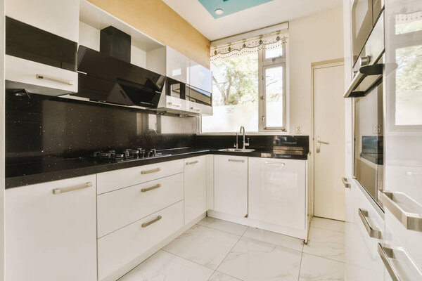 Fragment of interior of light narrow home kitchen with minimalist style white furniture with sink and stove