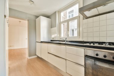 Gündüz vakti modern bir dairede yemek odasının yakınında modern dolaplar ve aletlerle donatılmış aydınlık mutfağın içi.