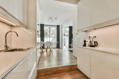 Çağdaş dairenin geniş odasındaki dinlenme odası ve mutfağın yakınındaki sandalyeli ve çiçekli masa.