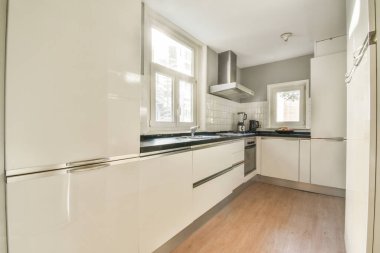 Gündüz vakti modern bir dairede yemek odasının yakınında modern dolaplar ve aletlerle donatılmış aydınlık mutfağın içi.