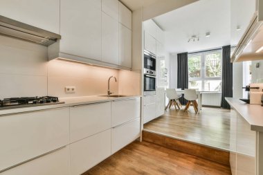 Çağdaş dairenin geniş odasındaki dinlenme odası ve mutfağın yakınındaki sandalyeli ve çiçekli masa.