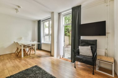 Çağdaş dairenin geniş odasındaki dinlenme odası ve mutfağın yakınındaki sandalyeli ve çiçekli masa.