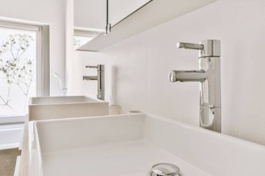 Çağdaş dairenin küçük fayanslı banyosunda lavabo ve duş arasında bulunan sifon tuvaleti